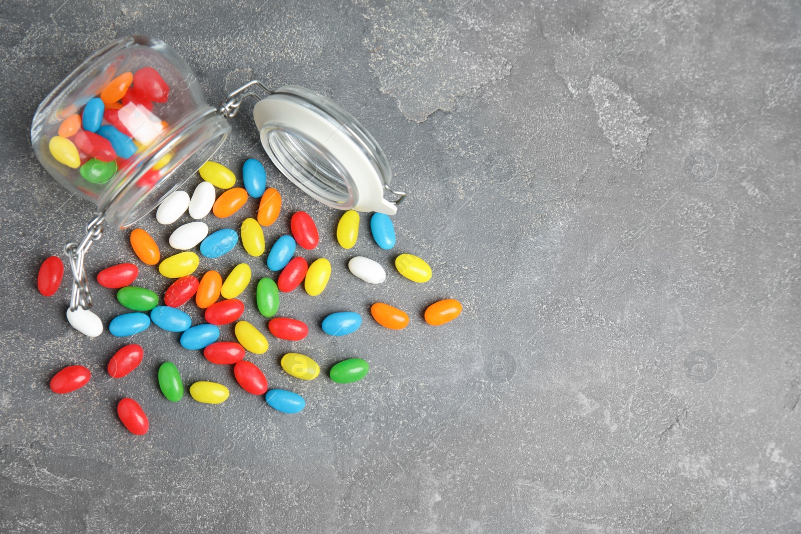 Photo of Overturned jar with jelly beans on stone background, top view. Space for text