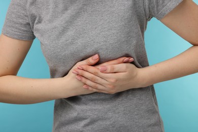 Photo of Woman suffering from stomach pain on light blue background, closeup