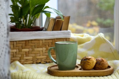 Photo of Cup of tasty hot drink and cookies near books on windowsill. Autumn coziness
