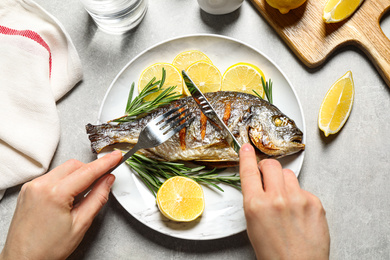 Photo of Woman eating delicious roasted fish at grey table, top view