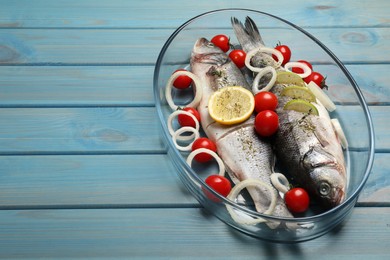 Photo of Glass baking tray with sea bass fish and ingredients on light blue wooden table. Space for text