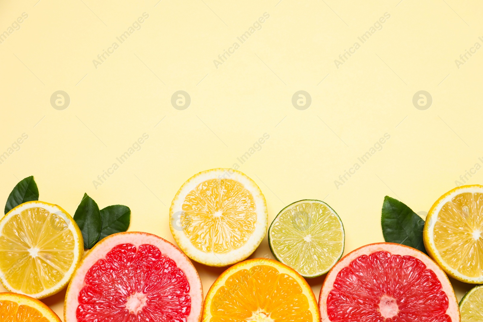 Photo of Different cut citrus fruits and leaves on beige table, flat lay. Space for text