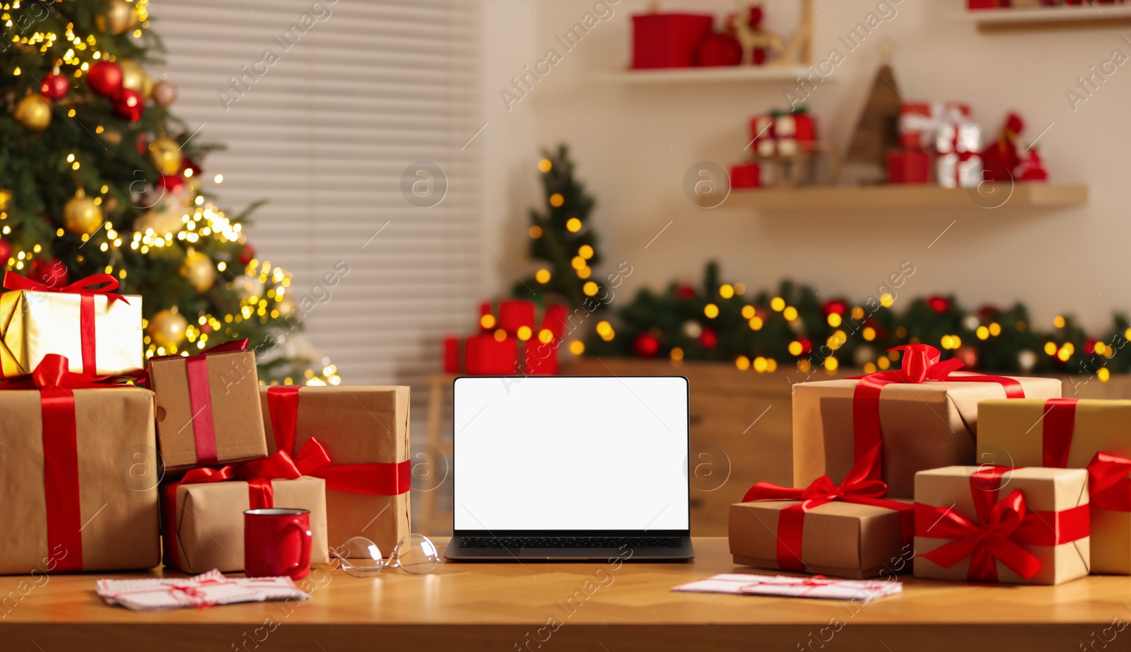 Photo of Christmas time. Laptop with blank screen, gift boxes and letters on table at home