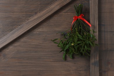 Photo of Mistletoe bunch with red bow hanging on wooden wall, space for text. Traditional Christmas decor