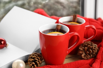 Photo of Cups of hot winter drink with knitted sweater on window sill indoors