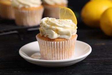 Photo of Delicious lemon cupcakes with white cream on black wooden table, closeup