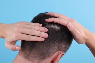 Man examining his hair and scalp on light blue background, closeup