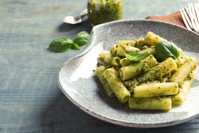 Plate with delicious basil pesto pasta on wooden table