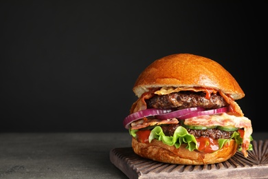 Photo of Tasty burger with bacon on table against black background. Space for text