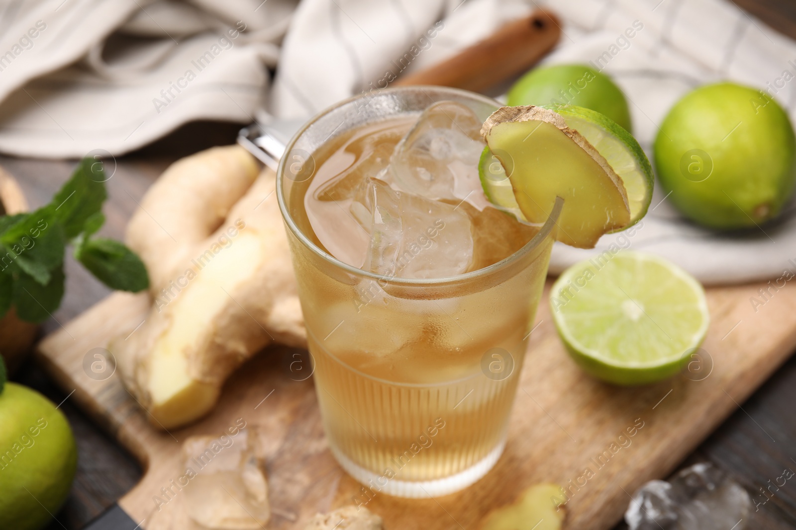 Photo of Glass of tasty ginger ale with ice cubes and ingredients on wooden table, closeup