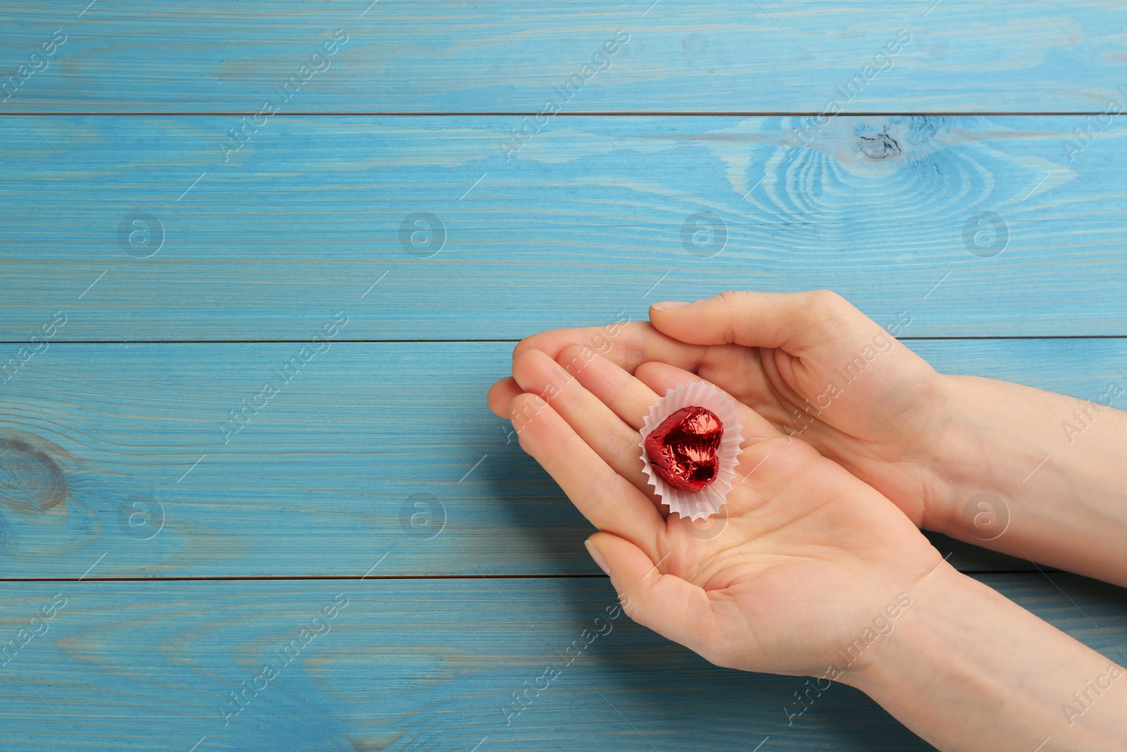 Photo of Woman holding heart shaped chocolate candy at blue wooden table, top view with space for text. Valentine's day celebration