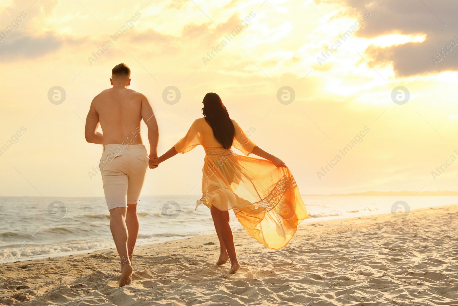 Photo of Lovely couple running together on beach at sunset, back view