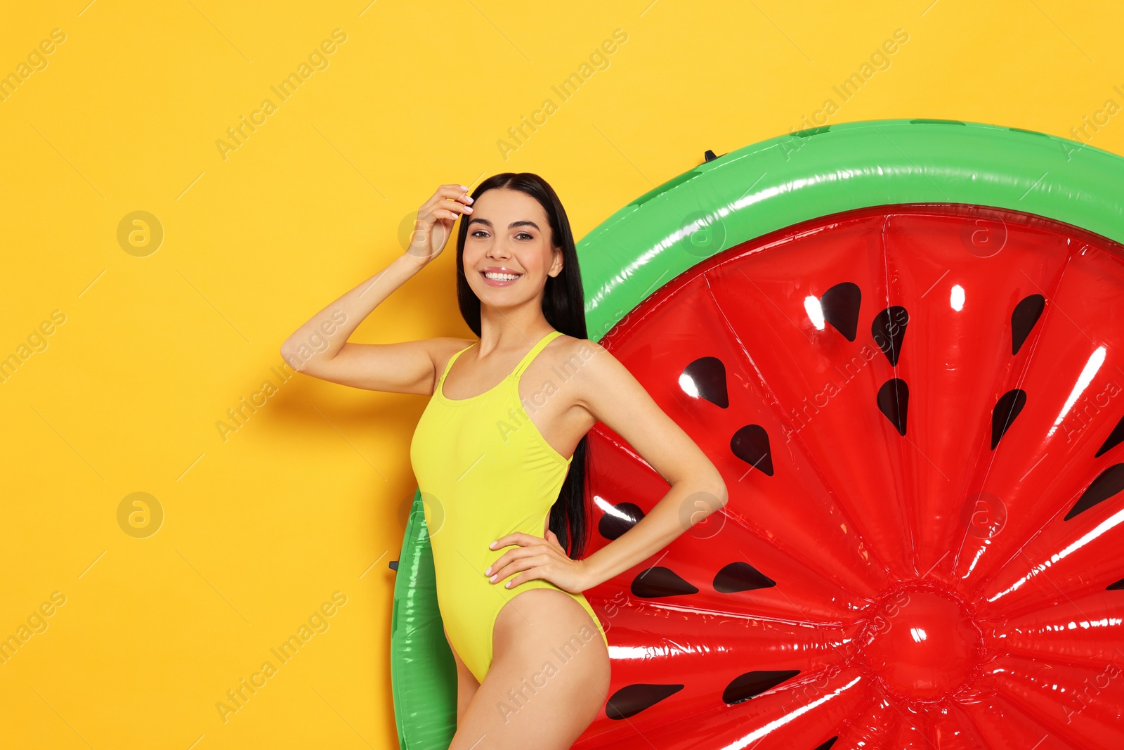 Photo of Young woman in stylish swimsuit near inflatable mattress against orange background