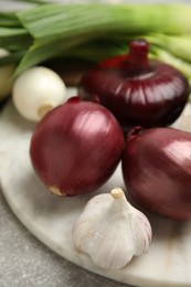 Fresh onion bulbs, leek and garlic on grey table, closeup