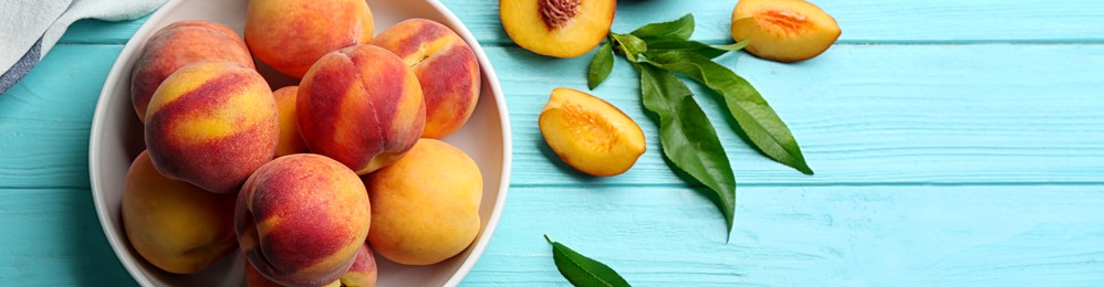 Image of Fresh ripe peaches and green leaves on light blue wooden table, flat lay. Banner design with space for text