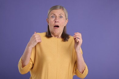Portrait of surprised senior woman on violet background