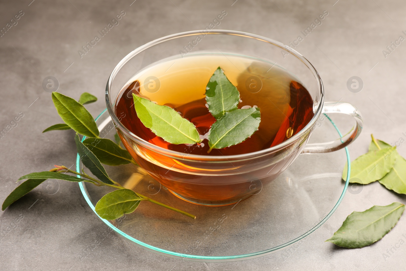 Photo of Cup of freshly brewed tea with bay leaves on grey table, closeup