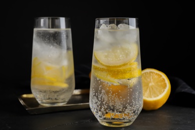 Photo of Soda water with lemon slices and ice cubes on black table