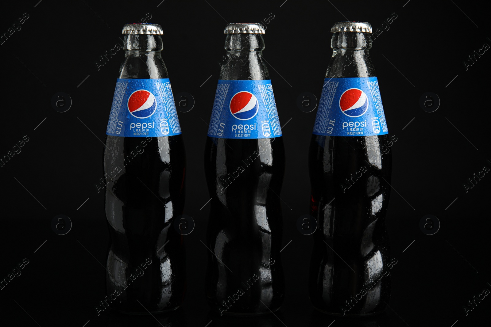 Photo of MYKOLAIV, UKRAINE - FEBRUARY 08, 2021: Glass bottles of Pepsi with water drops on black background