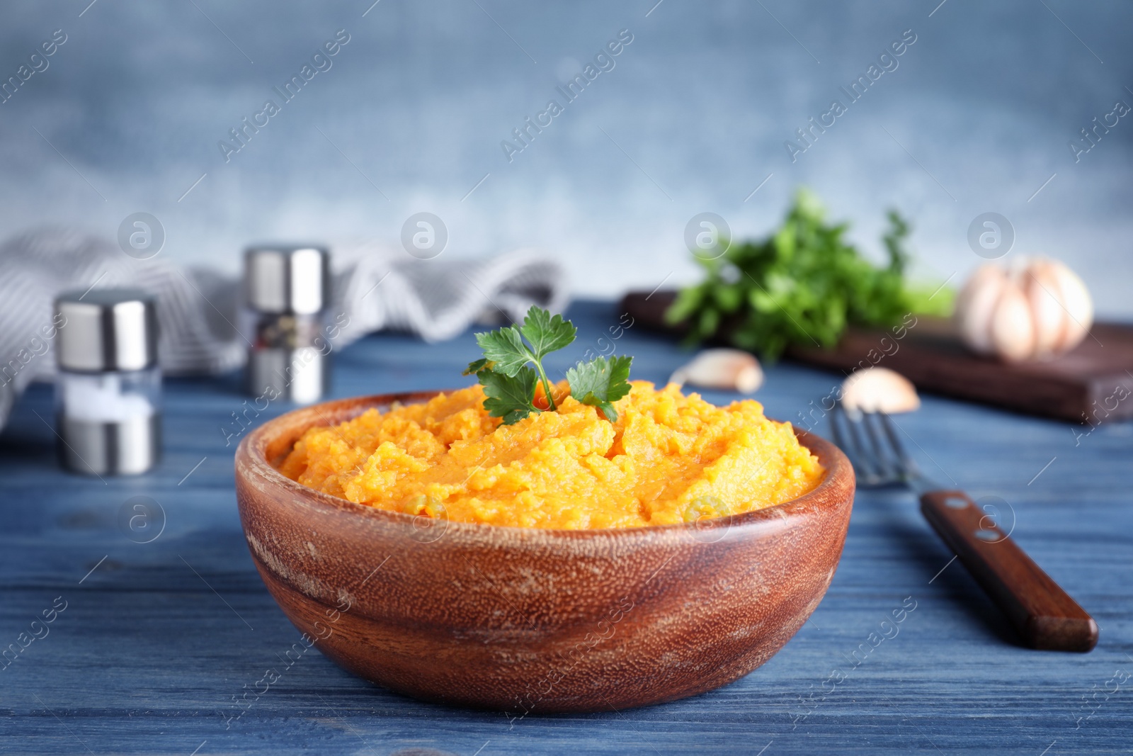 Photo of Bowl with mashed sweet potatoes on wooden table against color background. Space for text