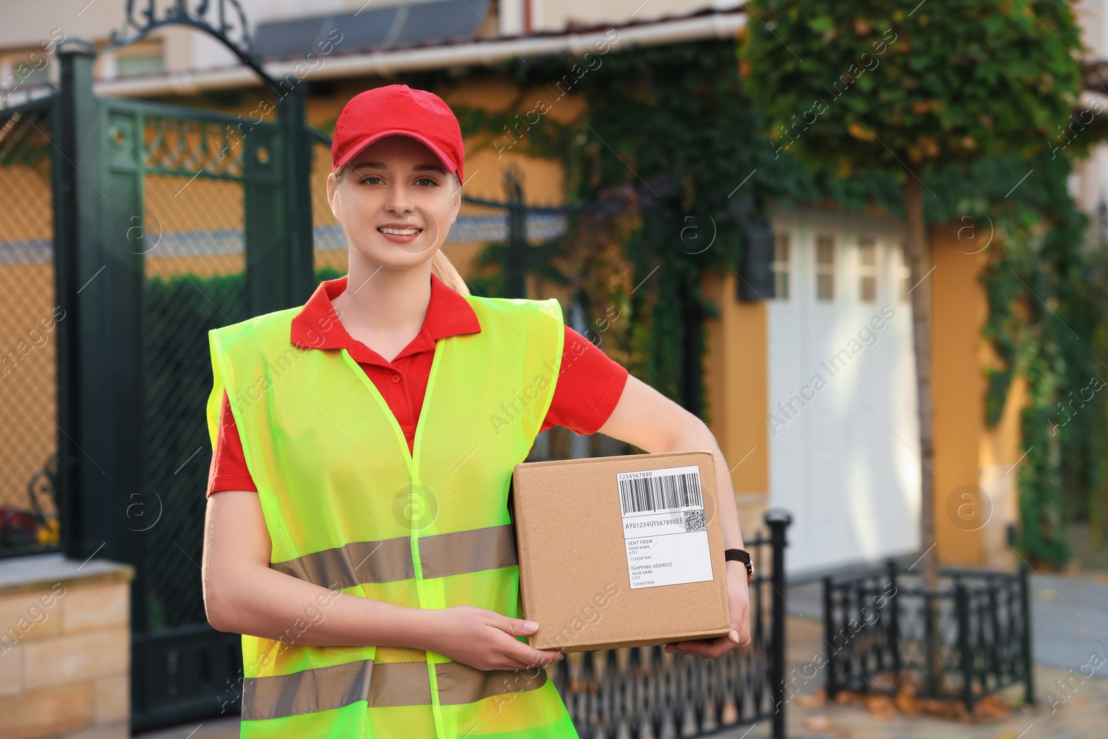 Photo of Courier in uniform with parcel near private house outdoors