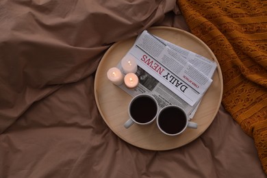 Cups of hot drink and candles on bed with brown linens, above view