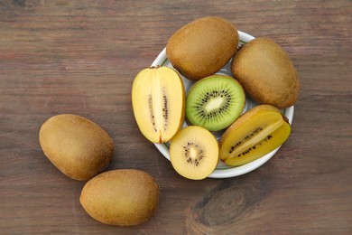 Photo of Plate with many whole and cut fresh kiwis on wooden table, flat lay