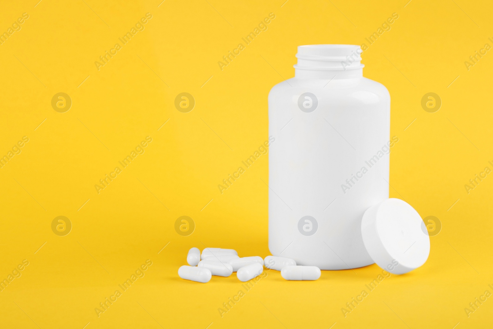 Photo of Blank white jar with vitamin capsules on yellow background, space for text