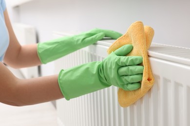 Photo of Woman cleaning radiator with rag indoors, closeup