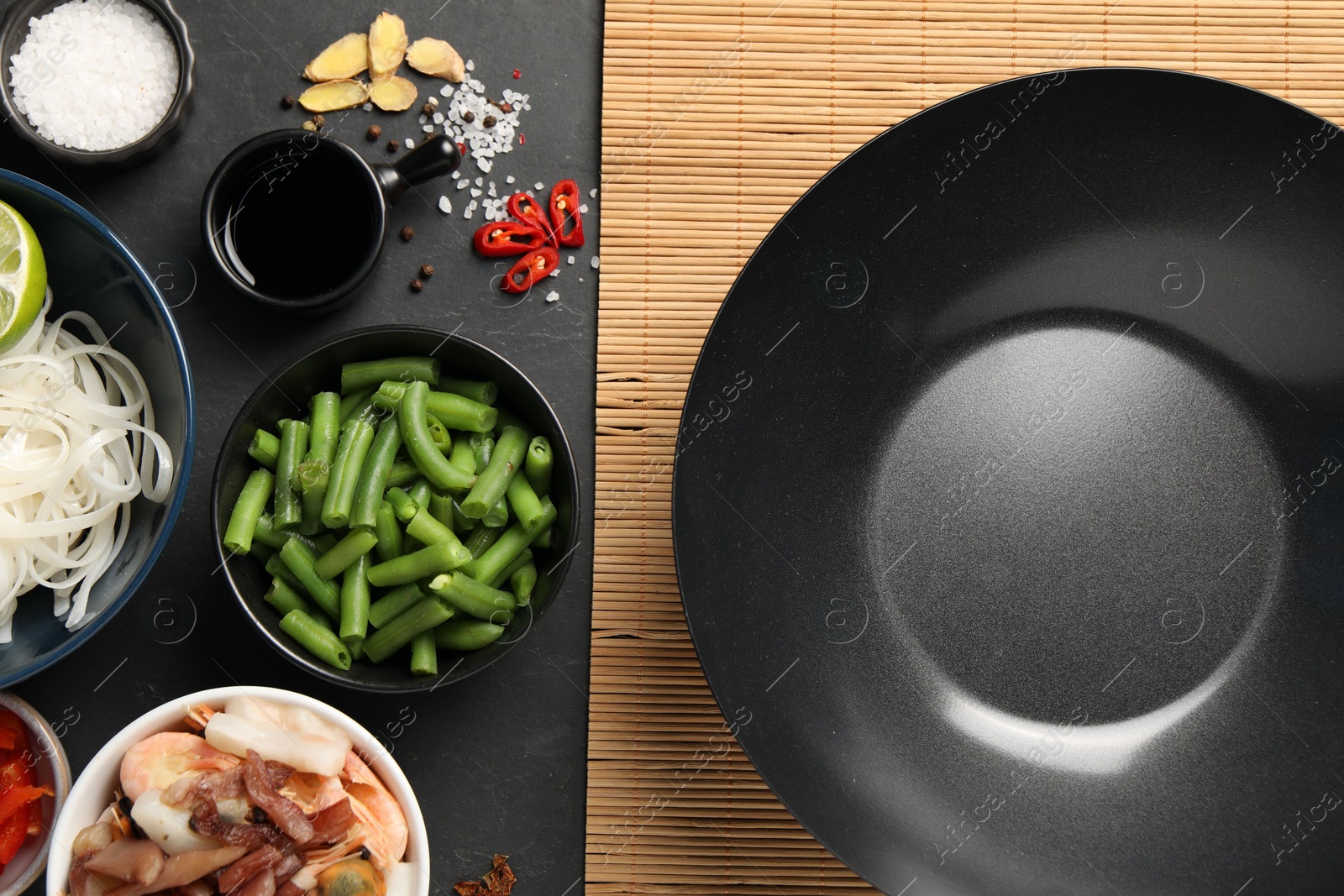 Photo of Flat lay composition with black wok, spices and products on dark textured table