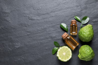 Photo of Glass bottlesbergamot essential oil and fresh fruits on black slate table, flat lay. Space for text