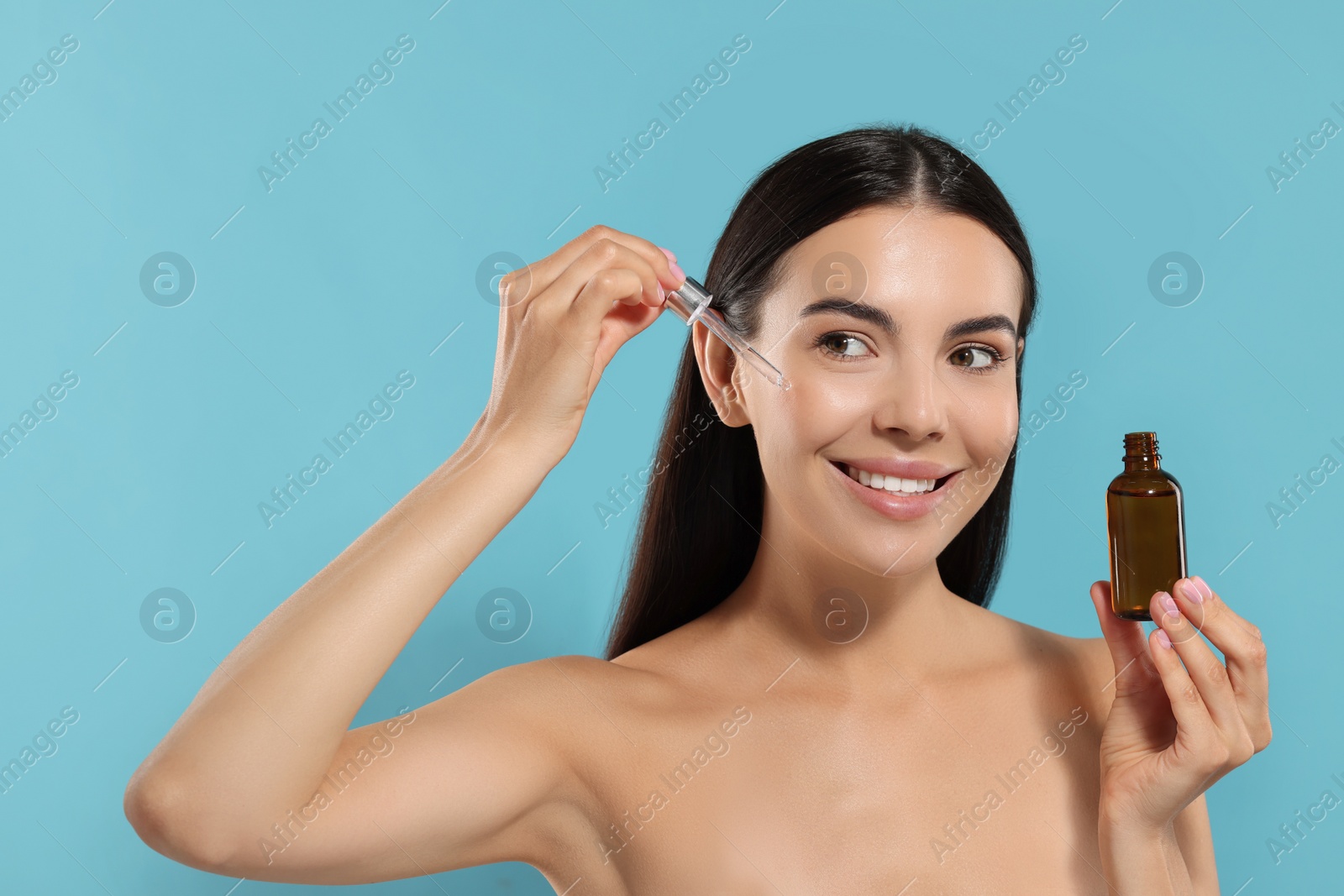 Photo of Beautiful young woman applying serum onto her face on light blue background