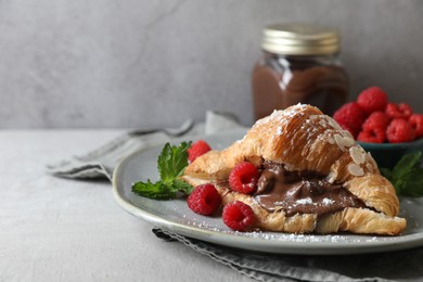 Photo of Delicious croissant with chocolate and raspberries on light grey table, space for text