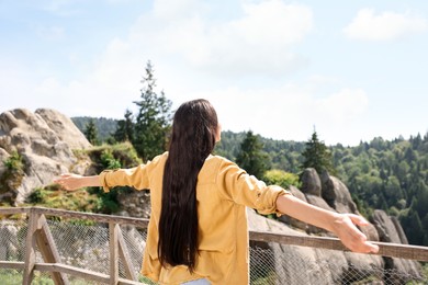 Photo of Feeling freedom. Woman with wide open arms near wooden railing in mountains, back view