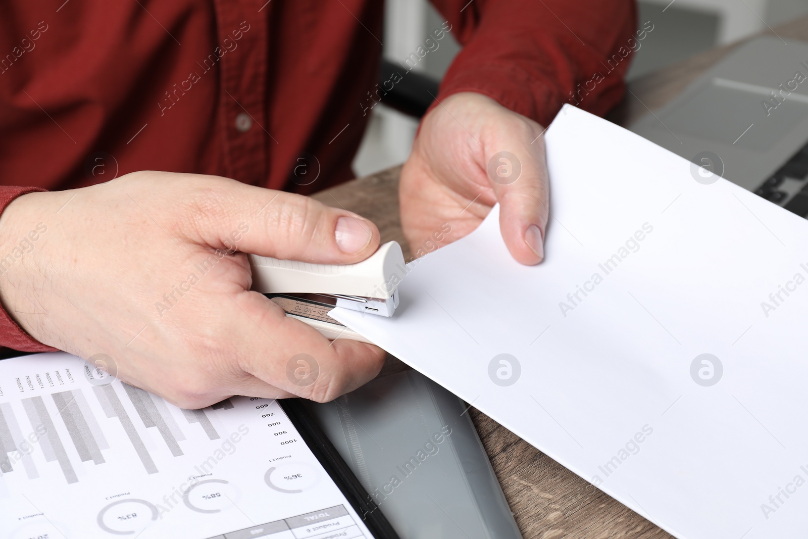 Photo of Man with papers using stapler at wooden table, closeup