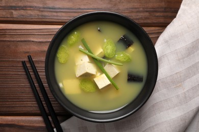 Photo of Bowl of delicious miso soup with tofu served on wooden table, top view