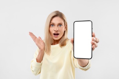 Surprised woman holding smartphone with blank screen on white background