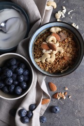 Photo of Tasty granola in bowl, blueberries and yogurt on gray textured table, flat lay