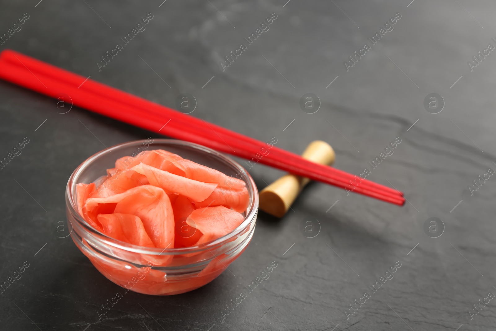 Photo of Spicy pickled ginger and chopsticks on black table, space for text