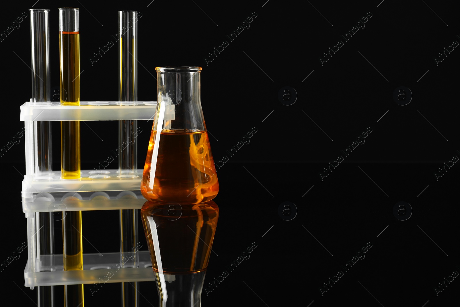 Photo of Laboratory glassware with different types of oil on black background. Space for text