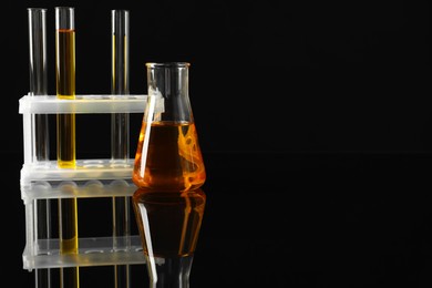 Laboratory glassware with different types of oil on black background. Space for text