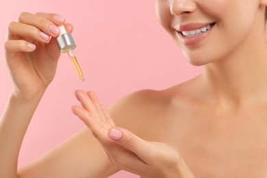 Young woman applying serum onto her hand on pink background, closeup