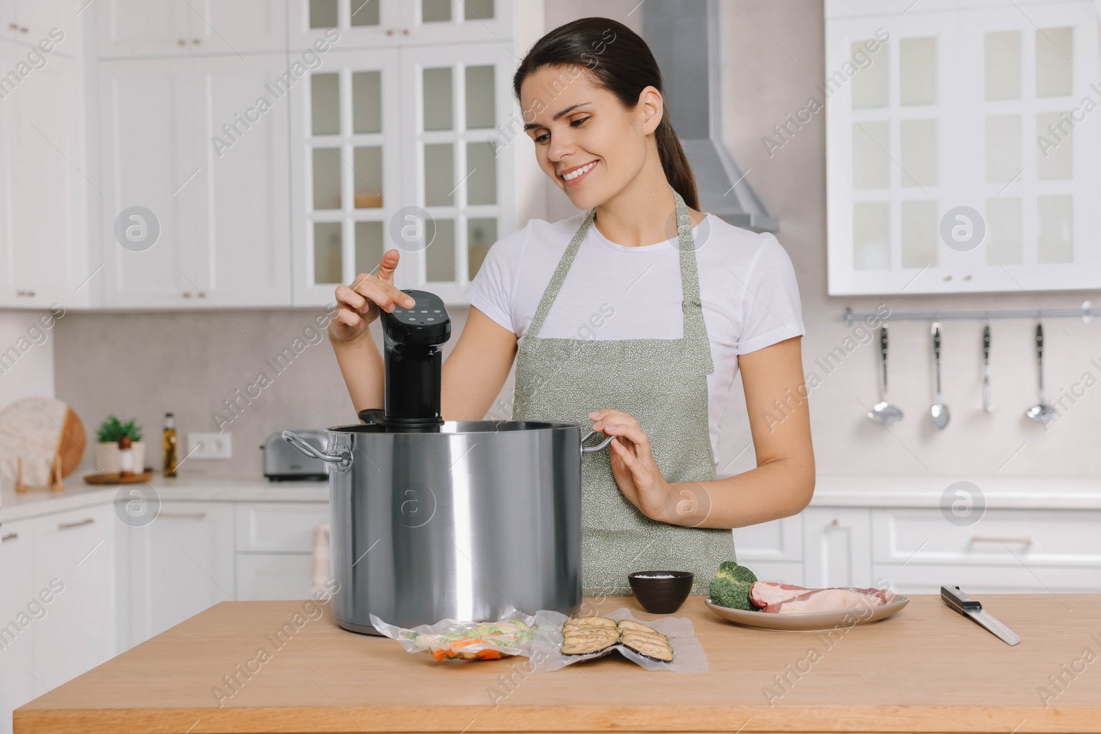 Photo of Woman using thermal immersion circulator at table in kitchen. Sous vide cooking