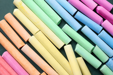 Photo of Pieces of color chalk on greenboard, flat lay