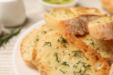 Tasty baguette with garlic and dill on white table, closeup