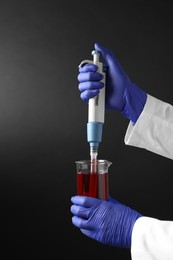 Photo of Laboratory analysis. Scientist dripping sample with micropipette into beaker on dark background, closeup