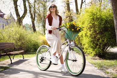 Beautiful woman with bicycle and bouquet of yellow tulips outdoors on sunny spring day