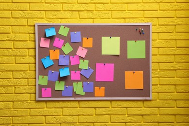 Corkboard filled with colorful notes and pins on yellow brick wall