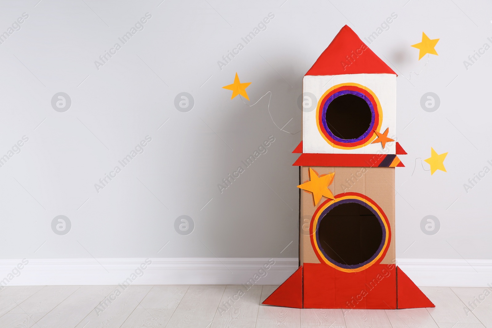 Photo of Cute handmade cardboard spaceship near light wall. Space for text