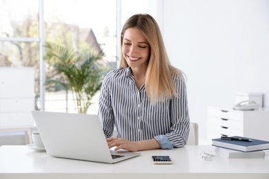 Young businesswoman using laptop at table in office